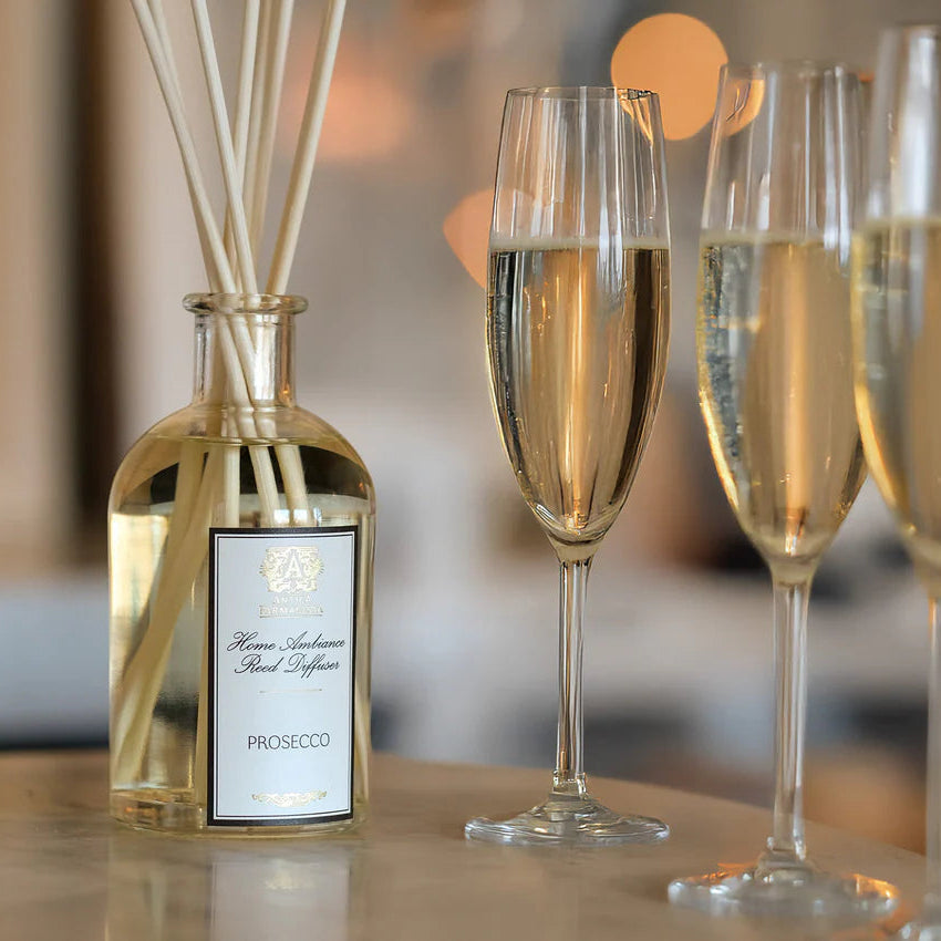 Prosecco bottle with reeds and three glasses of Prosecco on a table.