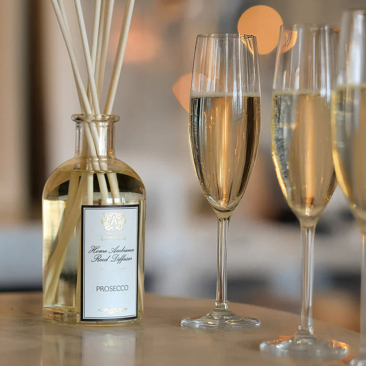 Prosecco bottle with reeds and three glasses of Prosecco on a table.