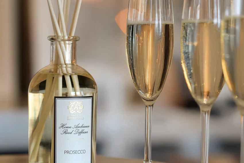 Prosecco bottle with reeds and three glasses of Prosecco on a table.